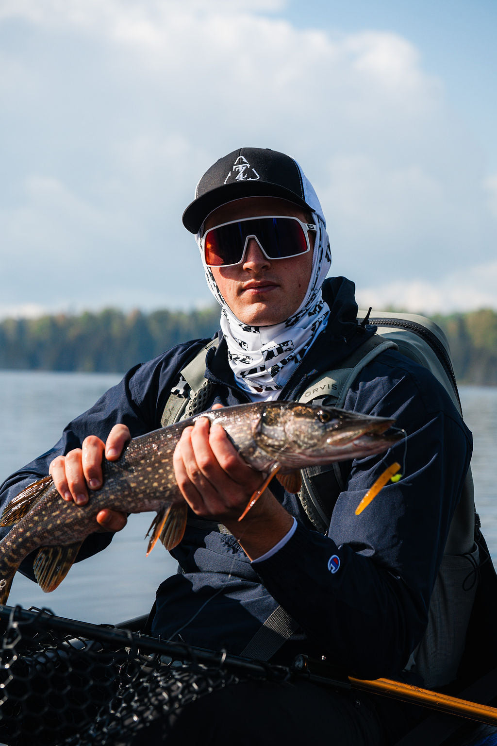A professional photo of a model wearing Zero Trace Baits clothing holding a Northern Pike